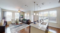 This well-appointed two-bedroom, two-bathroom residence in Spring, Texas is designed with an open-concept layout that maximizes both space and functionality. Rich wood-style flooring flows throughout the main living areas, anchoring the bright and airy atmosphere created by multiple large windows dressed with blinds and curtains.

The living room serves as a central gathering space, featuring a ceiling fan, neutral-toned walls, and generous natural light from a bank of windows with outdoor views. It connects seamlessly to the kitchen and dining area, creating a cohesive and inviting flow. The kitchen is equipped with dark espresso cabinetry, granite countertops, stainless steel appliances including a range, microwave, and dishwasher, and a large island with pendant lighting that doubles as a dining bar.

Both bedrooms offer comfortable proportions, plush carpeting, ceiling fans, and ample closet space. The primary bedroom includes an en-suite bathroom featuring a soaking tub, hardwood-style flooring, a spacious walk-in closet, and a dark-cabineted vanity. The second bathroom mirrors the quality finishes with a tub-shower combination and dark overhead cabinetry. A hallway entry connects all areas efficiently, completing this thoughtfully designed single-story residence.