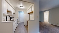 Located at 26011 Lakeshore Blvd in Euclid, Ohio, this single-floor residence offers two bedrooms and one bathroom within a practical and well-organized layout. The kitchen is designed for efficiency, featuring white cabinetry — both upper and lower — light countertops, a stainless steel sink with a matte black pull-down faucet, and a white electric coil range. Wood-look flooring runs throughout the kitchen, which connects seamlessly to the living area via a half-wall partition. The living and dining area is carpeted and benefits from natural light through a large window fitted with vertical blinds, complemented by a ceiling fan overhead. A baseboard heating system runs along the perimeter walls. The generously sized primary bedroom features plush carpet, ample wall space, and a full-width closet with bi-fold doors, offering substantial storage. The second bedroom is also carpeted and bright. The bathroom is clean and functional, finished with white tile surrounding a tub-shower combination, a single-sink vanity with white cabinetry, a mirror, and wood-look flooring. The neutral color palette and straightforward design provide a move-in-ready living environment throughout the entire home.