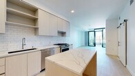 Located on the 17th floor in the heart of downtown San Diego (92101), this modern high-rise residence offers a thoughtfully designed single-level layout with clean contemporary aesthetics throughout. Light-toned hardwood flooring flows seamlessly across the open-concept living and kitchen areas, creating a cohesive and airy atmosphere.

The kitchen is a standout feature, equipped with a large waterfall-edge quartz island, flat-front cabinetry in warm wood and matte finishes, white subway tile backsplash, and a full suite of stainless steel appliances including a gas range, refrigerator, built-in microwave, and dishwasher. Ample upper cabinetry with open shelving provides generous storage.

The living area opens directly to a private balcony through floor-to-ceiling black-framed glass doors, filling the space with natural light and offering sweeping views of the San Diego skyline and surrounding cityscape. Exposed concrete structural columns add an industrial accent against the crisp white walls.

Bedrooms feature the same light hardwood flooring, large windows with city views, built-in shelving, and barn-style sliding doors. The primary bathroom is finished with large-format white tile flooring, a double vanity with quartz countertops, backlit mirrors, wood cabinetry with brushed gold hardware, and a soaking tub alongside a tiled shower surround.