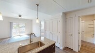 This single-floor residence offers a thoughtfully designed open-concept layout that seamlessly connects the kitchen, dining, and living areas. The kitchen serves as the centerpiece, anchored by a granite-topped island with an undermount sink, dark espresso cabinetry, pendant lighting, and black stainless appliances including a range, microwave, and refrigerator. Recessed lighting and track lighting further illuminate the workspace. The adjacent living area features wood-style plank flooring, a ceiling fan, and sliding glass doors that open to a private balcony with outdoor views, allowing generous natural light to fill the space.

Built-in shelving in the living area provides practical storage and display options. A bedroom features plush carpeting, a ceiling fan, a large window, and its own sliding glass door access to an outdoor balcony. An additional carpeted room with its own entry offers flexible use as a second bedroom or office. The bathroom is finished with a dark wood vanity topped with granite, an undermount sink, and wood-style flooring. Throughout the unit, a neutral color palette, clean white walls, and consistent finishes contribute to a cohesive, modern aesthetic.