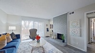 This single-floor residence offers a well-designed layout with distinct living, dining, sleeping, and kitchen areas. The living room serves as the focal point of the home, anchored by a painted brick fireplace that extends to the ceiling and complemented by wood-style flooring. Large sliding glass doors flood the space with natural light while providing access to a private balcony with outdoor views. A dedicated dining nook adjacent to the living area features a pass-through opening to the kitchen, creating an open and connected feel.

The galley-style kitchen is finished with white shaker cabinetry, light countertops, subway tile backsplash, wood-style flooring, and stainless steel appliances, including a refrigerator and range. A window above the sink brings in additional natural light.

The primary bedroom is a comfortable retreat with plush carpeting, a ceiling fan, and a walk-in closet with built-in organization. A secondary bedroom offers carpeted flooring and generous wall space. The bathroom features white cabinetry, a wide vanity with a clean countertop, wood-style flooring, and a tiled tub-shower combination.