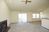 This single-floor home offers a well-organized layout designed for comfortable everyday living. The open living area is an immediate highlight, featuring soaring vaulted ceilings, a ceiling fan, and a tile-surround fireplace that serves as a natural focal point. A sliding glass door fills the space with natural light and provides direct access to an outdoor area. The kitchen is laid out in a practical galley configuration, equipped with warm oak cabinetry, white appliances including a range, refrigerator, dishwasher, and built-in microwave, along with light-toned countertops and durable tile flooring. A peninsula counter connects the kitchen to the main living area, creating an open, connected feel. Two carpeted bedrooms offer a quiet retreat, each featuring ceiling fans and windows that bring in natural light. The home includes two full bathrooms, both finished with tile flooring, vanity cabinetry, and tub-shower combinations. One bathroom features a large vanity mirror and slatted wood accent panel, adding a touch of warmth. Throughout the home, neutral tones, consistent trim work, and practical finishes create a clean, cohesive aesthetic.