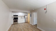 This single-floor unit offers a clean, functional layout designed for comfortable everyday living. The open kitchen and living area forms the heart of the space, showcasing crisp white shaker-style cabinetry, a full suite of stainless steel appliances including a gas range, over-the-range microwave, and a full-size refrigerator, along with a single-basin sink with a modern brushed nickel faucet. Light wood-style luxury vinyl flooring runs throughout, providing a warm, cohesive look that ties the spaces together seamlessly. Neutral beige walls create a calm, versatile backdrop throughout the unit. The living area is generously sized with room for a variety of furniture arrangements and includes a dedicated entryway with a panel door and a window fitted with horizontal blinds, allowing for natural light and ventilation. A wall-mounted HVAC unit provides climate control convenience. The bedroom is a quiet, comfortable retreat featuring a window with blinds that invite soft, diffused natural light. The bathroom is outfitted with a full tub-and-shower combination, accented by clean white tile surround. The textured ceiling throughout adds a subtle architectural detail, while recessed lighting in the kitchen ensures bright, practical illumination. The overall design is modern, freshly updated, and move-in ready.