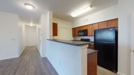 This single-story residence offers a practical and well-organized layout spread across multiple rooms. The open-concept living and kitchen area serves as the heart of the home, where wood-look hard-surface flooring extends throughout, creating a cohesive and easy-to-maintain space. The kitchen is defined by warm medium-toned wood cabinetry with arched detailing, dark countertops, and a full suite of black appliances, including a refrigerator, electric range, and over-the-range microwave. A peninsula with matching countertop separates the kitchen from the living area, offering additional workspace and a casual dining option. A dedicated laundry room is conveniently accessible directly from the kitchen, housing a full-sized washer and dryer. The bedrooms feature soft wall-to-wall carpeting and windows fitted with horizontal blinds, allowing natural light to filter in while maintaining privacy. Each room is finished with clean white walls and neutral tones, contributing to a bright, move-in-ready atmosphere. Multiple bathrooms are present throughout, each equipped with a full soaking tub and shower combination set against clean white surrounds. Ceiling fans are installed throughout the living and sleeping areas, enhancing comfort and air circulation across the home.