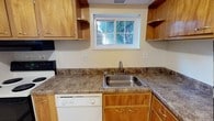 This single-floor residential space offers a practical and comfortable layout with a clean, neutral aesthetic throughout. The kitchen is well-appointed with warm honey-toned wood cabinetry, including both upper and lower cabinets as well as open shelving for additional storage. Laminate countertops in a stone-like finish provide generous workspace, complemented by a stainless steel sink, a white dishwasher, and an electric range. A window above the sink frames views of lush greenery outside, bringing in natural light and a pleasant connection to the outdoors.

The living area is open and airy, finished with neutral wall-to-wall carpeting and crisp white walls that create a bright, inviting atmosphere. A pass-through opening connects this space to the kitchen, enhancing the sense of openness and flow between rooms. The bedrooms continue the same neutral carpeted flooring and feature horizontal band windows positioned along the upper walls, allowing natural light to filter in while maintaining privacy. Baseboard heating units run along the walls, ensuring efficient warmth throughout. A wall-mounted air conditioning unit in one room provides year-round climate control. Each room offers a clean canvas with ample space and a calm, understated ambiance throughout the unit.