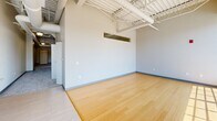 Located at 2599 Church Ave in Cleveland, OH, this four-bedroom, two-bathroom unit offers an impressive loft-style aesthetic across a single floor. The open-concept living and kitchen area immediately commands attention with soaring ceilings featuring exposed structural beams, ductwork, and industrial-style pendant lighting. Large floor-to-ceiling windows flood the space with abundant natural light, while warm hardwood-style flooring anchors the main living area. The kitchen is thoughtfully equipped with rich wood cabinetry, granite countertops, stainless steel appliances including a range, microwave, dishwasher, and refrigerator, and a generous central island that provides additional prep and seating space. The four bedrooms are carpeted for comfort, each benefiting from the unit's characteristically tall ceilings and ceiling fans. The spacious primary bedroom features dual closets for ample storage. The two bathrooms are finished with granite-topped wood vanities and tile flooring; one includes a walk-in shower while the other offers a full tub-shower combination with a curved curtain rod. A hallway connects the private sleeping quarters to the main living spaces, creating a functional and cohesive layout throughout.