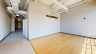 Located at 2599 Church Ave in Cleveland, OH, this four-bedroom, two-bathroom unit offers an impressive loft-style aesthetic across a single floor. The open-concept living and kitchen area immediately commands attention with soaring ceilings featuring exposed structural beams, ductwork, and industrial-style pendant lighting. Large floor-to-ceiling windows flood the space with abundant natural light, while warm hardwood-style flooring anchors the main living area. The kitchen is thoughtfully equipped with rich wood cabinetry, granite countertops, stainless steel appliances including a range, microwave, dishwasher, and refrigerator, and a generous central island that provides additional prep and seating space. The four bedrooms are carpeted for comfort, each benefiting from the unit's characteristically tall ceilings and ceiling fans. The spacious primary bedroom features dual closets for ample storage. The two bathrooms are finished with granite-topped wood vanities and tile flooring; one includes a walk-in shower while the other offers a full tub-shower combination with a curved curtain rod. A hallway connects the private sleeping quarters to the main living spaces, creating a functional and cohesive layout throughout.