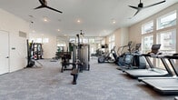 Located at 713 Adelynn Ln in Greensboro, NC, this dedicated fitness center offers a generously proportioned, single-floor exercise space designed to support a comprehensive range of workout routines. The room is finished with durable, textured carpet flooring and features crisp white walls that create a clean, motivating environment. Recessed lighting and multiple ceiling fans with pendant mounts ensure consistent illumination and comfortable airflow throughout the space.

Large windows line multiple walls, flooding the interior with natural light and providing views of the surrounding community. Full-length mirrors are strategically positioned to enhance the sense of openness and allow users to monitor their form during exercise.

The cardio zone is well-appointed with multiple treadmills, elliptical trainers, and stair climbers, all equipped with individual display screens. The strength training area includes a multi-station cable machine and a dedicated free weights section featuring a full rack of dumbbells and weight plates. A functional training station offers battle ropes, kettlebells, medicine balls, resistance bands, and a multi-purpose power rack for dynamic workouts.

The entry area features glass-paned double doors, a mounted flat-screen television, and a small amenity station, creating a welcoming transition into the fitness space. The overall layout is thoughtfully organized to accommodate multiple users simultaneously while maintaining clear circulation paths.