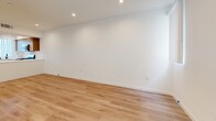 Located at 900 N Ardmore Ave in Los Angeles, CA, this three-bedroom, two-bathroom home spans three floors with a clean, modern aesthetic. The ground floor houses a spacious garage with a motorized door, recessed lighting, a tankless water heater, electrical panel, and a dedicated in-unit washer and dryer area with concrete flooring. The main living floor features an open-concept kitchen and living room with light wood flooring throughout. The kitchen is outfitted with stainless steel appliances including a gas range, microwave, dishwasher, and refrigerator, complemented by two-tone cabinetry — warm wood uppers and white lowers — over white quartz countertops and a peninsula for additional workspace. The living area is bright and open, with vertical blinds and natural light filtering through tall, narrow windows. The upper floor hosts three bedrooms, including a generously sized primary bedroom, and two bathrooms. The bathrooms feature wood-tone vanities with white quartz countertops, light wood-style tile flooring, and brushed nickel fixtures. All bedrooms are finished with the same light hardwood flooring, recessed lighting, and vertical blinds, creating a consistent, contemporary feel throughout the home.