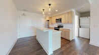 This single-floor residence at 510 Trailside Dr in Charlottesville, Virginia offers a thoughtfully designed layout with contemporary finishes throughout. The open-concept kitchen serves as a central highlight, featuring light maple cabinetry, white quartz countertops, and a full suite of stainless steel appliances, including a refrigerator, electric range, built-in microwave, and dishwasher. A generously sized kitchen island with an undermount sink and stylish pendant lighting overhead adds both functionality and visual appeal to the space.

Rich, dark hardwood flooring extends throughout the main living areas, creating a warm contrast against the crisp white walls and recessed lighting above. The living area is expansive and open, offering ample room for various furniture arrangements. A large sliding glass door floods the space with natural light and provides direct access to an outdoor balcony with open views of the surrounding Charlottesville landscape.

The bathroom features light tile flooring, a wood-toned vanity with white countertop, and a full soaking tub with shower combo. The overall design is clean and modern, maintaining a consistent neutral palette that gives the space a bright, airy ambiance throughout.