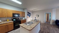 This single-floor residence offers a thoughtfully designed layout that balances functionality and comfort throughout. The kitchen is a standout feature, equipped with warm honey-toned cabinetry, granite-style countertops, and a full suite of black appliances including a gas range, built-in microwave, and refrigerator. A peninsula with a double-basin sink provides additional prep space and opens directly to the dining area, creating a seamless flow ideal for entertaining. The dining space is intimate yet well-proportioned, illuminated by adjustable track lighting and accented by contemporary wall art. The living room offers generous space, wood-style flooring, a ceiling fan, and a sliding glass door that invites natural light and outdoor views. The bedrooms are carpeted for comfort, each featuring large windows with ample natural light. One bedroom showcases a bold teal accent wall and a ceiling fan, while another offers serene neutral tones and garden views. The bathroom connects to a spacious walk-in closet outfitted with multi-tier wire shelving, providing excellent storage capacity. Wood-style flooring runs through the main living areas, tying the space together with a clean, cohesive aesthetic throughout.