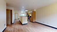 This single-floor residence offers a well-organized layout that balances open communal areas with private bedroom spaces. The heart of the home is an open-concept kitchen and living area, where light wood-style flooring extends throughout, creating a bright and cohesive feel. The kitchen is equipped with stainless steel appliances, including a refrigerator and range, complemented by warm honey-toned cabinetry that provides ample storage. A central island with a bold red countertop serves as a functional focal point, ideal for meal preparation or casual dining. Recessed lighting and flush-mount fixtures illuminate the space evenly, while windows allow natural light to filter in and offer views of surrounding greenery.

The bedrooms feature plush gray carpeting, cream-toned walls, and generous closet space with built-in wire shelving, providing practical storage solutions. The bathroom is appointed with a wide vanity offering substantial counter space and drawer storage, a large mirror, and wood-trimmed doorways that add a warm accent throughout. A dedicated in-unit laundry area with a stacked washer and dryer adds everyday convenience. Dark baseboards throughout the unit provide a clean, defined contrast to the light walls and flooring, lending the space a polished, finished appearance.