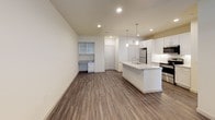 This well-appointed single-floor unit combines modern design with practical functionality throughout its thoughtfully designed layout. Dark hardwood-style flooring flows seamlessly throughout, creating a cohesive and contemporary aesthetic.

The open-concept living and kitchen area serves as the heart of the space. The kitchen stands out with crisp white shaker-style cabinetry, granite countertops, and a large central island with an undermount sink — illuminated by stylish pendant lights. Stainless steel appliances, including a refrigerator, range, and over-the-range microwave, complement the geometric tile backsplash. A built-in desk nook is also visible in the living area, offering a dedicated workspace.

The living area is bright and open, with large windows fitted with blinds that allow natural light to fill the room, complemented by a ceiling fan overhead. A private entry door with sidelight windows adds to the welcoming feel.

The bedroom is generously sized, featuring a ceiling fan and a window with an exterior view, while the adjoining walk-in closet provides ample storage with multi-level shelving and hanging rods along the walls.

The bathroom is finished with elegant marble-look tile on both the floors and tub surround, a soaking tub with shower combination, and a clean white vanity with an undermount sink, creating a serene and polished retreat.