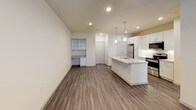 This well-appointed single-floor unit combines modern design with practical functionality throughout its thoughtfully designed layout. Dark hardwood-style flooring flows seamlessly throughout, creating a cohesive and contemporary aesthetic.

The open-concept living and kitchen area serves as the heart of the space. The kitchen stands out with crisp white shaker-style cabinetry, granite countertops, and a large central island with an undermount sink — illuminated by stylish pendant lights. Stainless steel appliances, including a refrigerator, range, and over-the-range microwave, complement the geometric tile backsplash. A built-in desk nook is also visible in the living area, offering a dedicated workspace.

The living area is bright and open, with large windows fitted with blinds that allow natural light to fill the room, complemented by a ceiling fan overhead. A private entry door with sidelight windows adds to the welcoming feel.

The bedroom is generously sized, featuring a ceiling fan and a window with an exterior view, while the adjoining walk-in closet provides ample storage with multi-level shelving and hanging rods along the walls.

The bathroom is finished with elegant marble-look tile on both the floors and tub surround, a soaking tub with shower combination, and a clean white vanity with an undermount sink, creating a serene and polished retreat.