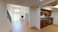 Located on Canoga Avenue in the Canoga Park neighborhood of Los Angeles, this two-story home offers a thoughtfully designed layout across both levels. The main floor makes an immediate impression with its dramatic soaring ceilings, visible from the open living area, which is anchored by a fireplace and framed by an arched transom window that draws in abundant natural light. Light-toned tile flooring flows throughout the main level, complementing the warm, neutral wall tones that carry throughout the home.

The kitchen is a functional galley-style space equipped with rich wood cabinetry, granite-style countertops, stainless steel appliances including a gas range and refrigerator, and a built-in sink — all finished with tile flooring that ties seamlessly into the main living areas. A striking wrought iron staircase leads to the upper level, where carpeted bedrooms provide a comfortable, quiet retreat. Each bedroom features vertical blinds allowing for natural light control.

The bathrooms are finished with tile flooring and include tub-shower combinations fitted with sliding glass doors. One bathroom features an adjoining walk-in closet with built-in shelving, adding practical storage. The overall ambiance is clean, bright, and move-in ready.