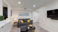 Located at 1238 W Adams Blvd in Los Angeles, this single-floor unit offers a clean, contemporary design with a cohesive neutral palette and light wood-style flooring that flows seamlessly throughout every room. The open-concept living area provides a welcoming atmosphere, featuring recessed lighting and a comfortable layout centered around a charcoal sofa, glass-top coffee table, and bright yellow accent pieces that add a vibrant pop of color.

The kitchen is thoughtfully designed with dark cabinetry contrasted against light countertops, a mosaic tile backsplash, and stainless steel appliances including a gas range, over-the-range microwave, and refrigerator. A peninsula with a built-in sink and seating extends into the common area, creating a natural connection between cooking and living spaces.

The bedroom accommodates twin beds flanked by dark nightstands, with a bright window allowing natural light to fill the room. Additional built-in cabinetry provides convenient storage near a hallway utility area.

The bathroom features a full tub-shower combination with tiled surround, wood-style flooring, and clean white finishes, offering a simple and functional space. Overall, the unit presents a modern, well-appointed interior well-suited for its West Adams, Los Angeles location.