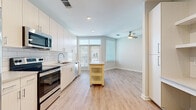 Located at 2020 W Morehead St in Charlotte, NC, this single-floor unit offers a bright, contemporary layout designed for comfortable everyday living. The open-concept kitchen and living area serves as the heart of the space, featuring light wood-style flooring that extends throughout. The kitchen is outfitted with stainless steel appliances — including a range, microwave, and dishwasher — complemented by light-toned cabinetry, a white subway tile backsplash, and ample counter space. A movable kitchen island provides additional prep and storage flexibility. Natural light fills the living area through large windows with blinds, while a ceiling fan overhead adds practical comfort. The bedroom offers a quieter atmosphere with plush carpeting underfoot and a distinctive horizontal clerestory window that introduces a unique architectural detail and additional natural light. The bathroom is finished with a light wood-grain vanity, quartz-style countertops, a large mirror, and a subway tile tub-shower surround, maintaining the clean, modern aesthetic found throughout the unit. Overall, the space presents a cohesive, light-filled environment with consistent finishes and a functional, well-organized floor plan.