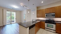 Located at 2323 Dulles Station Blvd in Herndon, Virginia, this single-floor residence offers a well-designed open-concept layout with modern finishes throughout. The kitchen serves as a central focal point, featuring warm honey-toned cabinetry, dark granite countertops with subtle veining, and a white subway tile backsplash. A peninsula with an undermount sink and pendant lighting overhead connects the kitchen to the living area, creating a seamless flow. Stainless steel appliances, including a gas range, built-in microwave, and refrigerator, complete the functional cooking space. Light tile flooring grounds the kitchen, transitioning into hardwood-style flooring that extends throughout the main living areas. The living space benefits from natural light through sliding glass doors and windows that frame views of surrounding greenery. The bedroom is bright and airy, with a large window overlooking mature trees, providing a serene backdrop. The bathroom is well-appointed with white cabinetry, a dark granite vanity top, an undermount sink, and a combined shower and soaking tub with tile surround. An adjacent closet with built-in shelving adds practical storage. Overall, the space balances contemporary finishes with a comfortable, functional design.
