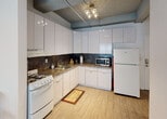 Located at 953 Collins Ave in the heart of Miami Beach, FL, this single-floor unit offers an urban industrial aesthetic defined by its striking exposed concrete beam ceilings, which serve as a defining architectural feature throughout the space. The flooring transitions seamlessly between wood-look tile and laminate planks, providing a warm contrast to the raw overhead structure.

The living area is bright and open, benefiting from natural light streaming through a large window dressed with vertical blinds. The room accommodates a comfortable seating arrangement alongside a wall-mounted flat-screen TV set above a wood-and-metal media console, creating a functional yet contemporary atmosphere.

The kitchen is well-equipped with glossy white cabinetry that extends to the ceiling, dark granite-style countertops with a tile backsplash, a gas range, microwave, and a full-size refrigerator — offering ample storage and prep space for everyday use.

The bedroom features exposed concrete beams overhead, crisp white walls, and a built-in closet with sliding doors, providing practical storage. The full bathroom is clean and functional, finished with wood-look tile flooring, a white vanity with mirrored medicine cabinet, and bright vanity lighting. A hallway connects the rooms, accented by a full-length framed mirror and track lighting beneath the exposed structural ceiling elements.