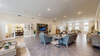 The Residences at Potomac Crest clubhouse is a thoughtfully designed, single-floor community amenity building that offers a welcoming and functional environment for its residents. The entry foyer greets visitors with herringbone-patterned tile flooring, crown molding, and glass double doors that open to an outdoor patio, flooding the space with natural light.

The expansive main lounge serves as the heart of the clubhouse, featuring the same distinctive herringbone tile, recessed lighting, and elevated ceilings with crown molding throughout. Comfortable seating arrangements anchored by area rugs create an inviting atmosphere, while a built-in media center with a large flat-screen TV provides a focal point for gatherings. Glass-paned French doors lead to a private office or workstation area, offering a quiet retreat within the open layout.

The conference room is a polished, dedicated meeting space appointed with a large rectangular table, ergonomic mesh chairs, carpeted floors, and natural light from a window overlooking greenery. Decorative wall art and metallic accents lend a refined, professional tone.

The well-equipped kitchen features rich dark cabinetry, white countertops, stainless steel appliances, a coffee station, and a breakfast bar with upholstered seating — ideal for community events and casual gatherings. A secondary prep kitchen provides additional counter space and storage, completing this versatile and elegantly appointed clubhouse.