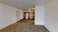 This single-floor residence features three bedrooms and three bathrooms, offering a practical and well-organized layout suited for a variety of living arrangements. The open-concept living and kitchen area forms the heart of the home, where the two spaces flow seamlessly together. The living area is finished with neutral wall-to-wall carpeting, creating a warm and understated atmosphere, while the kitchen transitions to hard-surface flooring for easy maintenance. The kitchen is equipped with warm-toned wood cabinetry that provides ample storage, complemented by white appliances including a refrigerator and a freestanding range with an overhead ventilation hood. The clean white walls throughout lend the interior a bright, neutral canvas that adapts easily to personal décor. A door from the main living area provides convenient access, likely to a utility or exterior entry point. The overall design is straightforward and functional, emphasizing usability and ease of living. With three full bathrooms to serve the three bedrooms, this residence is well-suited for shared living or families seeking practicality and sufficient space across a single cohesive level.