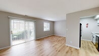 This 2-bedroom, 1-bathroom apartment at Vineyards Apartments in Indianapolis, Indiana offers a practical and well-appointed single-floor layout. The living room is a bright, welcoming space featuring light wood-look flooring, neutral taupe walls, and a sliding glass door flanked by vertical blinds that floods the room with natural light and provides outdoor views. A secondary window further enhances the airy feel of the space. A pass-through opening connects the living area to the kitchen, which is designed as a galley-style space with white cabinetry featuring black hardware, marble-look countertops, a black industrial-style faucet, and black appliances including a refrigerator and range. The second bedroom offers light wood flooring and includes a closet, while the spacious primary bedroom is carpeted and features two generous closets—one with sliding doors—providing ample storage. A natural-light window brightens the primary bedroom. The full bathroom is outfitted with a tub/shower combination featuring crisp white surrounds and matte black fixtures. Neutral tones, clean finishes, and a functional layout define the overall character of this comfortable apartment home.