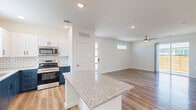This well-appointed two-story home offers five bedrooms and three bathrooms across a thoughtfully designed layout. The main floor serves as the heart of the home, featuring an open-concept kitchen and living area filled with natural light. The kitchen is a standout space, boasting a central island with granite countertops, two-tone cabinetry with white upper cabinets and deep navy-blue lower cabinets, a classic white subway tile backsplash, and a full suite of stainless steel appliances. Light wood-look flooring flows throughout the main level, complementing the bright, neutral palette. Ceiling fans provide comfort in the living areas, while sliding glass doors lead to an outdoor space. A convenient half bathroom is located on the main floor near the entry. Upstairs, the secondary bedrooms feature plush carpeting and natural light from well-placed windows. The primary bedroom offers generous space, and closets throughout include built-in shelving and hanging rods for organized storage. The bathrooms are finished with granite-topped vanities, brushed nickel fixtures, and tub-shower combinations. The home's clean, modern aesthetic, open layout, and functional design make it a comfortable and practical living space.