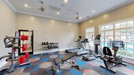 Located at Village Center Blvd in Fairburn, GA, this dedicated fitness center offers a comprehensive workout environment within a single, efficiently designed space. The room is finished with neutral warm-toned walls, classic crown molding, and recessed lighting complemented by dual ceiling fans, creating a comfortable and well-ventilated atmosphere. A bold, geometric-patterned carpet in shades of blue, orange, and gray covers the floor, adding a dynamic visual energy to the space.

Large windows along multiple walls flood the interior with natural light and provide views of an outdoor pool area, enhancing the open and airy ambiance. The fitness center is outstandingly well-equipped, featuring multiple treadmills, elliptical trainers, a stationary bike with an integrated display screen, and a cable/multi-use strength training machine. A dedicated free weights section includes a tiered dumbbell rack, while additional equipment such as a weight bench, medicine ball rack, a boxing/reflex training machine, and a leg exercise station round out the offering. The space supports a wide range of workout routines, from cardio and strength training to functional fitness, making it a versatile and fully appointed facility for residents.