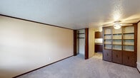 Located at 403 Rockdale Ave in Boardman, Ohio, this single-floor unit offers a practical and self-contained layout with one bedroom and one bathroom. The main living area is generously proportioned, featuring neutral beige walls, wall-to-wall carpet, dark wood baseboards, and a textured ceiling. A wall-mounted HVAC unit and a large window with blinds provide climate control and natural light, creating a bright and functional environment. The bedroom is notably spacious for the overall footprint of the unit, offering ample room for furnishings. It includes a built-in closet with bifold doors and double hanging rods, alongside a standalone dark wood shelving unit with cabinet storage below — ideal for organization and display. A ceiling fan with a light fixture adds both comfort and illumination. Adjacent to the bedroom, a compact kitchen area features dark wood cabinetry, a sink, and a stovetop, keeping essentials within easy reach. The bathroom is finished with neutral textured wall panels, chrome towel bars, a marble-topped vanity, and tile flooring, offering a clean and functional space. Overall, the unit presents a straightforward and efficient layout suited for single occupancy.