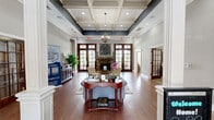 Located at 5605 Holly Grove Way in Knoxville, Tennessee, this well-appointed single-story community space offers a sophisticated and welcoming atmosphere across a generously sized floor plan. The grand entrance greets visitors with soaring ceilings, decorative white columns, arched doorways, and rich hardwood flooring that flows throughout the main areas. Elegant crown molding and a tray ceiling with dark accent detailing add architectural distinction to the main living room, which features a stone fireplace, large French doors, and abundant natural light from oversized arched windows. Classic tufted seating and warm, curated décor complete the inviting ambiance. The dining room offers a carpeted, intimate setting with an arched window, recessed lighting, and refined furnishings ideal for gatherings. The kitchen is equipped with warm wood cabinetry, granite countertops, hardwood floors, and an arched window that draws in natural light. The office space is bright and functional, lined with multiple arched windows and a French door providing outdoor access. A dedicated game room rounds out the amenity spaces, featuring a pool table, wall-mounted television, hardwood floors, and direct access to an outdoor patio through French doors — making it a lively hub for recreation and community engagement.