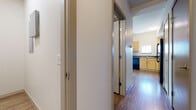 This single-floor residential unit offers a well-organized, functional layout designed for comfortable everyday living. Throughout the main living areas, warm wood-style flooring creates a cohesive and inviting atmosphere, extending from the open living space into the kitchen and hallways.

The kitchen is efficiently designed in an L-shaped configuration, featuring light maple cabinetry, dark countertops, a double-basin sink with a window above it, and a full suite of black appliances including a refrigerator, electric range, built-in microwave, and dishwasher. A pendant light overhead adds a subtle decorative touch.

The living area is bright and airy, benefiting from large sliding glass doors that open onto a private outdoor balcony, offering pleasant views of surrounding greenery and filling the interior with abundant natural light.

The bedroom spaces include a carpeted room with a large window that brings in natural daylight, as well as an additional room with sliding door access to the balcony and wood-style flooring. The bathroom is appointed with a wood-toned vanity, dark countertop, a grab bar, and a soaking tub, all set over durable wood-look flooring. A hallway with bifold doors connects the various areas of the unit, providing practical storage solutions throughout.