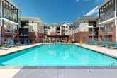 Located at 2000 Monroe Dr NE in Atlanta's vibrant Piedmont Heights neighborhood, this outdoor amenity space centers around a generously sized resort-style swimming pool that serves as the focal point of the community. The pool features crystal-clear turquoise water and is framed by a well-maintained concrete and tile deck, lined with bright blue lounge chairs that invite residents to relax and soak in the Atlanta sunshine.

The courtyard layout is thoughtfully designed, with the pool situated within a U-shaped arrangement of multi-story residential buildings. These buildings combine classic red brick facades at their base with contemporary siding, large windows, and private balconies on the upper levels — creating an architectural blend of traditional and modern styles. A decorative pergola anchors one end of the pool area, providing a shaded gathering spot that adds character and functionality to the outdoor space.

Lush mature trees and carefully maintained landscaping surround the perimeter, offering natural greenery that softens the built environment and provides additional shade. The space is enclosed by a sleek iron fence, ensuring privacy and security for residents. Abundant natural light floods the entire area throughout the day, making this outdoor space both inviting and practical for year-round enjoyment in Atlanta's warm climate.