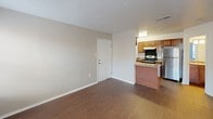 This single-floor residence offers a practical and well-organized layout visible across its living, kitchen, bedroom, and bathroom areas. The kitchen is equipped with stainless steel appliances, including a gas range and a full-size refrigerator, complemented by warm-toned wood cabinetry providing ample storage. Granite-style countertops and an under-cabinet range hood add functional detail, while overhead fluorescent lighting keeps the space well-lit. A peninsula counter separates the kitchen from the adjacent living area, creating a natural open-plan flow.

The living area features dark wood-style laminate flooring and neutral-toned walls, with multiple windows fitted with white horizontal blinds allowing natural light to fill the room. A textured popcorn ceiling runs throughout the main living spaces. The bedroom continues the neutral color palette, with plush carpeting underfoot, a ceiling fan with integrated light fixture, and windows on two walls that provide additional natural light and ventilation.

The bathroom includes a full-size soaking tub with an overhead shower, surrounded by classic white square tile extending fully up the walls, finished with chrome fixtures. Overall, the space maintains a clean, functional aesthetic suitable for everyday living.