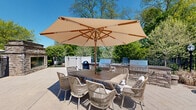 Located at 116 Danbury Rd in Wilton, Connecticut, this thoughtfully designed outdoor amenity space offers a welcoming environment with a range of functional and recreational features. The grounds are meticulously landscaped, incorporating mature deciduous trees, tall arborvitae hedges, and fresh mulched planting beds that provide both visual appeal and natural privacy screening along the perimeter. A black wrought-iron fence and gated entry further define the boundaries of the space while maintaining an open, airy feel. At the heart of the outdoor area lies a dedicated children's playground equipped with a multi-level play structure, slides, and open mulched surfacing for safe play. Comfortable park-style benches are positioned nearby, offering a place for supervision and relaxation. The space also includes a single-story utility or amenity building clad in shingle siding with a classic architectural roofline, accessible via a broad paved walkway. Under bright, open skies, the entire grounds benefit from abundant natural light, and the surrounding tree canopy provides shade and a sense of seclusion. An outdoor patio or gathering area with a pergola structure is also visible, rounding out the space as a versatile community-oriented destination.