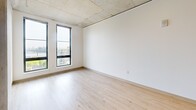 Located at 2045 SW River Parkway in Portland, Oregon, this one-bedroom, one-bathroom unit offers a well-designed layout with modern industrial touches throughout. The open-concept living and kitchen area features striking exposed concrete ceilings, light wood flooring, and large black-framed windows that fill the space with natural light and frame elevated views of the Portland cityscape and river beyond.

The kitchen is appointed with warm wood cabinetry, light countertops, a peninsula with an integrated sink, a dishwasher, electric range, and a full-size refrigerator — all complemented by a teal accent wall that adds a pop of color. The peninsula seamlessly connects the kitchen to the living area, creating an efficient and social layout.

The bedroom is a comfortable retreat, carpeted underfoot with a walk-in closet featuring wire shelving for ample storage. A second closet in the hallway provides additional organization space. Tall windows in the bedroom offer sweeping views of the city and river, making for a bright and inspiring atmosphere.

The bathroom includes a full tub-shower combination, a wood-accented vanity with a clean countertop, and neutral finishes throughout. A hallway connects all areas of the unit, contributing to a logical and practical flow. This unit combines urban industrial design with functional living in a prime Portland riverside location.