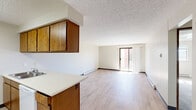 Located at 7007 N Nevada St in Spokane, WA, this one-bedroom, one-bathroom unit offers a practical and well-organized single-floor layout. The combined kitchen and living area forms the heart of the home, where light wood-style flooring runs throughout and a textured ceiling adds a classic touch. The kitchen features warm-toned wood cabinetry, a peninsula with a white countertop and built-in sink, and white appliances including a refrigerator and electric range — all under under-cabinet lighting. The living area is bright and open, with a sliding glass door that leads to a private balcony, inviting natural light deep into the space. Baseboard heating is present throughout, ensuring year-round comfort. The bedroom is carpeted for warmth and comfort, with a window that brings in natural light and views of the surrounding neighborhood. It includes access to a dedicated closet with a clothing rod. The full bathroom features white tile surround in the tub/shower combo, wood-style flooring, and clean, neutral finishes. A hallway connects the bedroom, bathroom, and closet to the main living areas, keeping the layout efficient and easy to navigate.