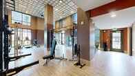 Located at 100 S 48th St in Phoenix, AZ, this single-floor fitness facility offers a thoughtfully designed space for comprehensive exercise and wellness activities. The layout encompasses a generously sized exercise room and a versatile living area, together delivering an expansive and functional environment.

The exercise room is a standout feature, boasting soaring double-height ceilings clad in warm wood paneling with a striking latticed ceiling detail. The space is outfitted with an extensive array of strength and cardio equipment, including cable machines, weight racks, benches, stair climbers, a rowing machine, and a full dumbbell rack. Large floor-to-ceiling windows flood the area with natural light while offering outdoor views, and full-length mirrors visually expand the space. Light hardwood-style flooring and a padded workout mat zone further enhance functionality.

The adjoining living area features the same soaring ceilings and light hardwood flooring, with a large wall-mounted display, a round backlit mirror, and wall-mounted speakers. Floor-to-ceiling sliding glass doors open directly to an outdoor area, creating a seamless indoor-outdoor connection. A dedicated functional training zone includes a TKO multi-rack system stocked with medicine balls and kettlebells. Throughout both spaces, the clean white walls and natural wood accents create a bright, modern, and motivating atmosphere.