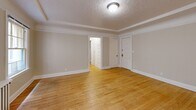 Located at 708 NW 19th Ave in Portland, Oregon, this one-bedroom, one-bathroom unit offers a well-organized layout across a single floor. The living room is a bright, open space characterized by warm hardwood floors, a decorative textured ceiling with crown molding, and classic cast-iron radiators that add a touch of historic charm. Multiple windows allow natural light to fill the room, offering views of the surrounding neighborhood. The layout flows naturally into an additional room, currently configured as a secondary living or dining area, which shares the same hardwood flooring and architectural detailing. The bedroom is a comfortable, private space with its own window for natural light and direct access to multiple closets, providing generous storage. The kitchen-dining area is efficiently designed, featuring white cabinetry with built-in open shelving, dark countertops, and hexagonal tile flooring. The full bathroom continues the clean aesthetic with a tiled tub-shower combination set within an arched alcove, a pedestal-style vanity, and matching hexagonal tile floors. A hallway connects the main spaces with additional closet storage. The unit's classic architectural details, including moldings and radiator heating, reflect its character-rich Portland heritage.