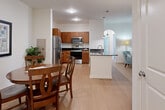 This well-appointed 3-bedroom, 2-bathroom model suite at 300 Summerchase St in Charles Town, WV offers a thoughtfully designed single-floor layout that balances comfort and functionality. The open-concept living area seamlessly connects the kitchen, dining room, and living room, creating an inviting and social atmosphere. The kitchen is equipped with warm-toned wood cabinetry, dark granite countertops, and a full suite of stainless steel appliances, including a refrigerator, electric range, and microwave. A central island with a built-in sink and pendant lighting adds both style and practicality. Light hardwood flooring runs throughout the main living areas, contributing to a bright, clean aesthetic. The dining area accommodates a round table for four and features an elegant arched entryway. A versatile office space offers natural light through large windows and provides a quiet, productive environment. The generously sized primary bedroom is carpeted and well-lit by natural light. Additional rooms include two more bedrooms and a dedicated office. The bathrooms are clean and functional, with one featuring a full soaking tub with grab bars. A built-in credenza area with dark granite counters adds additional storage and a refined touch to the layout.