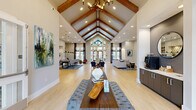 Located at 2720 Bristlecone Trail in Raleigh, NC, this impressive single-floor community space offers a thoughtfully designed interior that blends architectural elegance with functional versatility. The centerpiece of the space is a grand open living area crowned by a dramatic vaulted ceiling with exposed wooden beams and a striking multi-light chandelier. Light hardwood flooring runs throughout, complementing the neutral palette and enhancing the bright, airy atmosphere.

Large floor-to-ceiling windows and glass entry doors flood the interior with natural light while offering views of the surrounding exterior. The living room is anchored by a generous sectional sofa, contemporary accent chairs, and a shiplap-accented media wall with a mounted display. Two distinct dining areas provide flexible gathering options — one features a built-in banquette with a sculptural pendant light, while the other offers a cozy booth-style nook with curated wall art.

A dedicated office suite with glass-panel doors provides a professional workspace, while a built-in beverage station adds convenience to daily use. The hallways are generously proportioned, decorated with curated artwork, and connect each area seamlessly. The overall ambiance is modern yet warm, making this a welcoming and well-appointed communal facility.