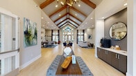 Located at 2720 Bristlecone Trail in Raleigh, NC, this impressive single-floor community space offers a thoughtfully designed interior that blends architectural elegance with functional versatility. The centerpiece of the space is a grand open living area crowned by a dramatic vaulted ceiling with exposed wooden beams and a striking multi-light chandelier. Light hardwood flooring runs throughout, complementing the neutral palette and enhancing the bright, airy atmosphere.

Large floor-to-ceiling windows and glass entry doors flood the interior with natural light while offering views of the surrounding exterior. The living room is anchored by a generous sectional sofa, contemporary accent chairs, and a shiplap-accented media wall with a mounted display. Two distinct dining areas provide flexible gathering options — one features a built-in banquette with a sculptural pendant light, while the other offers a cozy booth-style nook with curated wall art.

A dedicated office suite with glass-panel doors provides a professional workspace, while a built-in beverage station adds convenience to daily use. The hallways are generously proportioned, decorated with curated artwork, and connect each area seamlessly. The overall ambiance is modern yet warm, making this a welcoming and well-appointed communal facility.