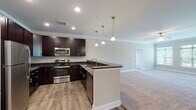 This single-floor residence offers a thoughtfully designed open-concept layout that seamlessly connects the kitchen and living area. The kitchen is a standout feature, showcasing rich dark-espresso cabinetry with brushed nickel hardware, dark granite countertops, stainless steel appliances including a gas range and built-in microwave, and a peninsula with pendant lighting that provides additional prep and seating space. The adjacent living area is finished with plush neutral carpeting and crown molding, creating a warm, cohesive atmosphere.

The bedrooms are generously sized, each featuring ceiling fans, soft carpeting, and ample natural light from windows with outdoor views. At least one bedroom includes a spacious walk-in closet with built-in shelving. The primary bedroom connects directly to an en-suite bathroom, while a second full bathroom serves the remaining rooms.

Both bathrooms are consistently appointed with dark vanity cabinetry, granite countertops, undermount sinks, framed mirrors, and tile flooring. The primary bath includes a walk-in shower with tile surround, while the secondary bath offers a tub-shower combination. Throughout the unit, crown molding, recessed lighting, and wood-look flooring in the kitchen tie together a refined, modern aesthetic.