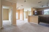 Located at 5505 Oxford Trace Way in Virginia Beach, Virginia, this single-floor residence offers a well-organized layout with a variety of thoughtfully designed living spaces. The kitchen is appointed with rich dark cherry wood cabinetry, dark granite-style countertops, hardwood-style flooring, and a full suite of black appliances including a refrigerator, range, and dishwasher. A centered window above the sink provides natural light, completing the U-shaped workspace. The living area features plush carpeting, crown molding, a ceiling fan, track lighting, and a large window that invites natural light. Multiple bedrooms throughout the home are finished with soft carpet, ceiling fans, and generously sized windows that frame outdoor views of surrounding greenery and the neighborhood. One bedroom includes a walk-in closet with built-in shelving, offering practical storage. Two bathrooms serve the home, each featuring rich hardwood-style flooring, white vanity cabinetry with ample drawer and cabinet storage, well-lit vanity mirrors, and clean, neutral wall tones. The overall aesthetic throughout is warm and neutral, with tan and beige tones creating a consistent and inviting ambiance across all rooms.