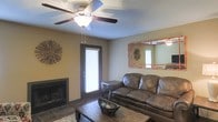 Located at 111 Lakeshore Dr. in Brandon, Mississippi, this single-floor home offers a welcoming and functional layout designed for comfortable living. The living room serves as the heart of the space, featuring a classic fireplace that anchors the room and provides a cozy focal point. Warm, neutral-toned walls create an inviting atmosphere, complemented by a ceiling fan with a built-in light fixture that ensures year-round comfort and ample illumination. A door with a windowed blind allows natural light to filter into the living area while maintaining privacy. The room accommodates generous seating, with rich leather sofas that add a warm, lived-in feel to the space. A rustic wooden coffee table grounds the seating area, and decorative wall accents, including a framed mirror and sunburst décor pieces, add character and visual interest. Tile flooring provides durability and easy maintenance in key areas, while a soft area rug defines the seating zone. The overall ambiance of the home is warm, casual, and well-appointed, making it a practical and comfortable retreat in the Brandon, Mississippi community.