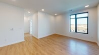 This contemporary single-floor residence showcases a clean, modern design with an open-concept layout that connects the kitchen and living areas seamlessly. The kitchen is a standout feature, equipped with a large center island topped with white quartz countertops, a matte black undermount sink with a matching faucet, stainless steel appliances including a French door refrigerator and electric range, a decorative tile backsplash, and a combination of white upper and dark wood lower cabinetry. Sleek linear pendant lighting above the island adds a polished finishing touch.

The living and dining areas are bright and airy, bathed in natural light from large, black-framed windows that frame open outdoor views. Light wood flooring runs throughout the main living spaces, complemented by recessed lighting overhead and crisp white walls that lend a fresh, neutral palette throughout.

The bedrooms continue the modern aesthetic, featuring the same large-format windows, with one room finished in plush carpeting. Both bathrooms are well-designed, with white cabinetry, white countertops, matte black hardware, and tile flooring. The primary bathroom offers an elongated vanity with ample storage. The overall ambiance is clean, bright, and move-in ready, reflecting a thoughtfully designed contemporary living space.