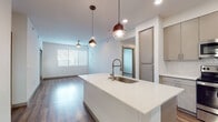 This thoughtfully designed single-floor residence combines modern aesthetics with functional living spaces. The open-concept layout seamlessly connects the kitchen and living area, creating an inviting and airy atmosphere. Rich hardwood-style flooring flows throughout the main living spaces, complemented by crisp white walls and recessed lighting.

The kitchen serves as a central hub, anchored by a spacious island with a quartz countertop and deep undermount sink, illuminated by stylish pendant lights. Taupe flat-front cabinetry lines the walls and extends to the ceiling for ample storage, while a full suite of stainless steel appliances — including a French door refrigerator, electric range, over-the-range microwave, and dishwasher — adds a sleek, professional touch. A white subway tile backsplash completes the look.

The living area is generously proportioned, bathed in natural light from large windows fitted with horizontal blinds, and finished with a ceiling fan overhead. The bedrooms feature plush carpeting, ceiling fans, and windows that bring in plenty of daylight. One carpeted bedroom offers a balcony-facing window with outdoor views.

The bathrooms are finished with quartz countertops, flat-front cabinetry, backlit vanity mirrors, and hardwood-style flooring. A tub-shower combination with clean white surrounds provides a crisp, modern feel throughout.