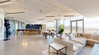 Located at 440 E Van Buren St in the heart of downtown Phoenix, this generously sized amenity floor delivers a sophisticated, open-plan environment designed for both comfort and collaboration. Polished concrete floors stretch throughout the interior, reflecting abundant natural light that pours in through dramatic floor-to-ceiling glass curtain walls, offering sweeping views of the Phoenix skyline and surrounding cityscape.

The main gathering area is anchored by multiple seating arrangements, including plush lounge sofas and accent chairs in warm earth tones, complemented by round dining tables with sculptural wooden chairs. A dedicated bar-style kitchen features a sleek white and wood-toned island with bar seating, a textured dark tile backsplash, and modern pendant lighting, providing a fully equipped social hub for residents or occupants.

A curved glass partition wall leads to a covered outdoor terrace, where exposed concrete ceilings and structural columns frame an alfresco lounge complete with white upholstered seating, a marble-topped coffee table, raised planters with lush greenery, and open views of the downtown skyline. An entry foyer with polished floors, wall-mounted artwork, and a credenza rounds out the space. Acoustic tile ceilings and linear LED lighting fixtures contribute to the refined, contemporary ambiance throughout.
