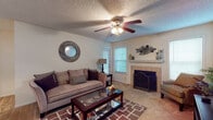 This single-story 1-bedroom, 1-bathroom model unit offers a well-organized layout designed for comfortable everyday living. The living room serves as the heart of the home, featuring a tile-surround wood-burning fireplace flanked by two windows that allow natural light to brighten the carpeted space. A ceiling fan with a light fixture provides year-round comfort, and textured ceilings are found throughout the unit. The kitchen is efficiently laid out with warm wood cabinetry, a electric range, and a full-size refrigerator, all set on durable tile-style flooring. A pass-through or open connection to the dining and living areas contributes to a functional flow throughout the home. The bedroom is generously sized with plush carpet flooring and features a sliding glass door that opens directly to a private outdoor patio, offering pleasant views of surrounding greenery. The full bathroom includes a tub-shower combination with classic white tile surround, a vanity with storage, and tile flooring. Throughout the unit, neutral tones and consistent finishes create a cohesive and inviting atmosphere, making this model an informative representation of the available floor plan.