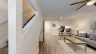 Located at 1301 E Central Ave in Bentonville, Arkansas, this two-story residence offers a thoughtfully designed layout with a clean, neutral aesthetic throughout. The main level features a welcoming living area with light hardwood-style flooring, a ceiling fan, and a built-in desk nook, creating a functional and comfortable gathering space. A staircase connects the two floors, with additional storage accessible beneath. The galley-style kitchen is well-appointed with white cabinetry, granite countertops, a stainless steel sink, track lighting, and black appliances including a refrigerator and range. A dedicated laundry area houses a full-size washer and dryer with overhead shelving for added storage convenience. The bathrooms feature granite-topped vanities with white cabinetry, undermount sinks, and gold or brushed nickel hardware accents. The upper level hosts multiple carpeted bedrooms, each equipped with ceiling fans. The primary bedroom includes a walk-in closet and an en-suite bath, while additional bedrooms offer closet space and natural light through blinded windows. Textured ceilings and crisp white walls are consistent throughout, lending a bright and well-maintained appearance to the entire home.