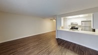 Located at 2636 Grand Avenue in the 92109 zip code of San Diego, this single-floor residence offers a well-organized layout with functional living spaces throughout. The open-concept living and dining area is finished with durable wood-look vinyl plank flooring and features a ceiling fan with light fixture, a textured ceiling, and a sliding glass door fitted with vertical blinds that allows natural light to fill the room. The kitchen is positioned adjacent to the living area behind a raised breakfast bar counter finished in light quartz-style laminate with a stainless steel sink. The kitchen itself is equipped with white cabinetry, stainless steel appliances including a refrigerator and electric range, an overhead range hood, and a recessed skylight-style ceiling panel that brightens the workspace. A hallway connects the main living area to the private quarters, where the bedroom features plush carpet flooring, a window with vertical blinds, and a wide sliding-door closet with a full-width hanging rod. The bathroom includes a combination shower and soaking tub with a curtain rod setup, chrome fixtures, and clean white surrounds. A vanity area with a light countertop, mirror, and towel ring completes the bathroom space. Clean white walls and consistent finishes throughout give the home a fresh, move-in-ready appearance.